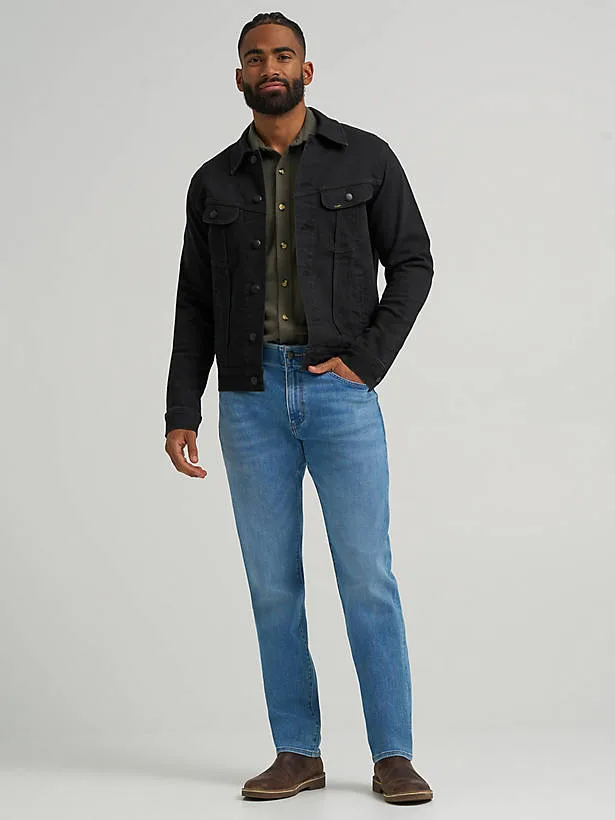 Male model wearing athletic fit blue jeans with extra thigh room and a tapered leg.