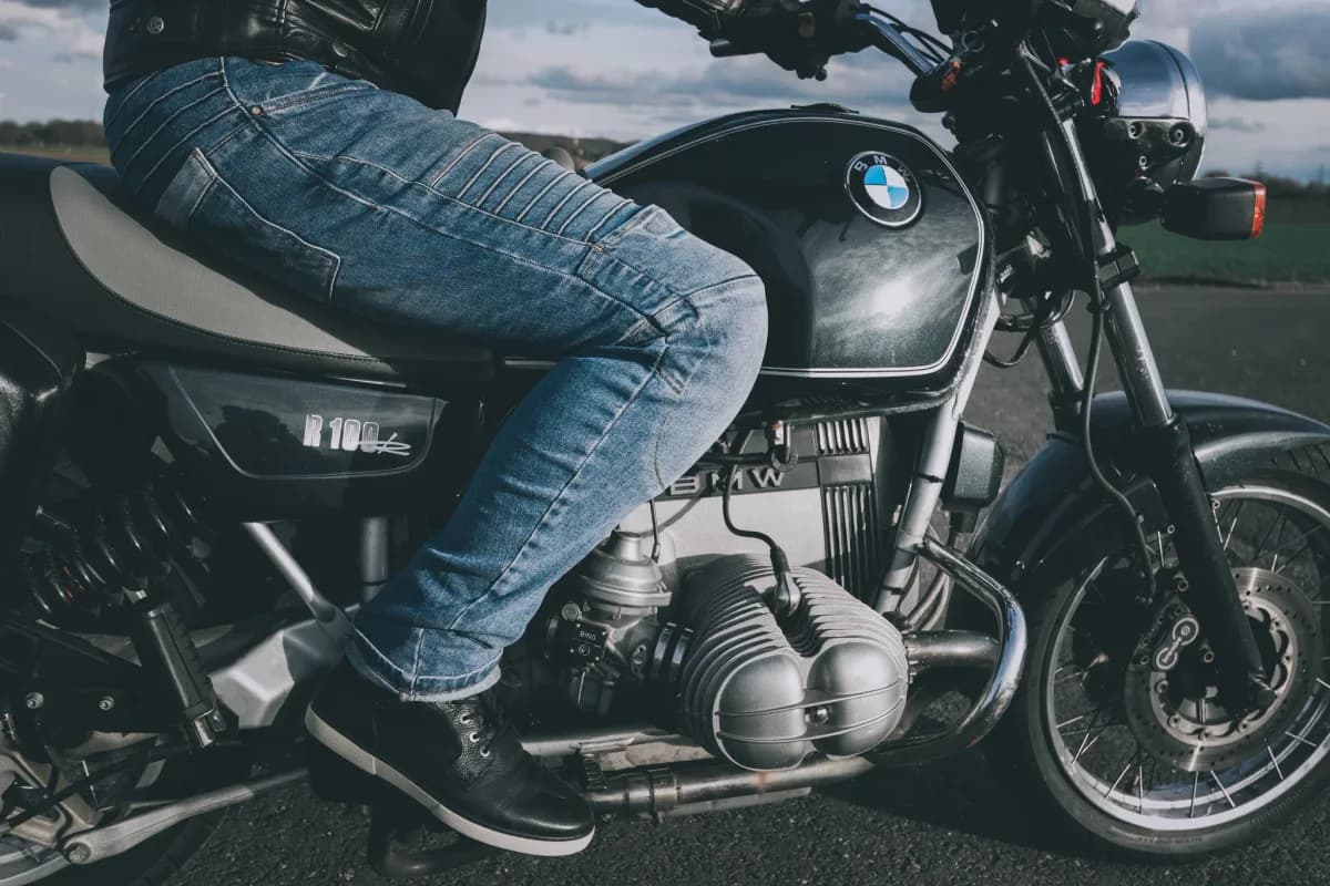 Motorcycle rider wearing protective denim jeans beside a motorcycle.