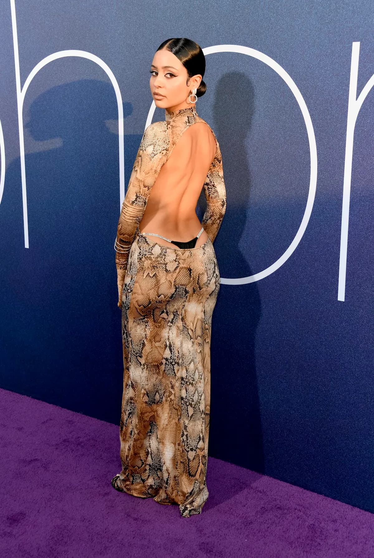 Alexa Demie in a snakeskin backless gown with exposed rhinestone thong straps.