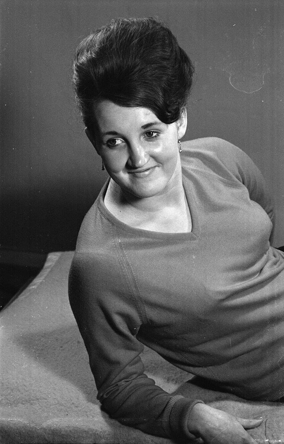 Archival photograph of a woman adopting a posing stance, featuring a large, structurally rigid, lacquered beehive updo.