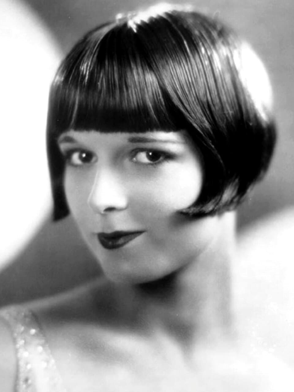 Archival studio photograph of silent film star Louise Brooks demonstrating the classic, razor-sharp 1920s French bob with a dense, perfectly straight fringe.